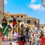 Folla festante durante una tradizionale festa patronale in Italia, con bancarelle e bandiere colorate.