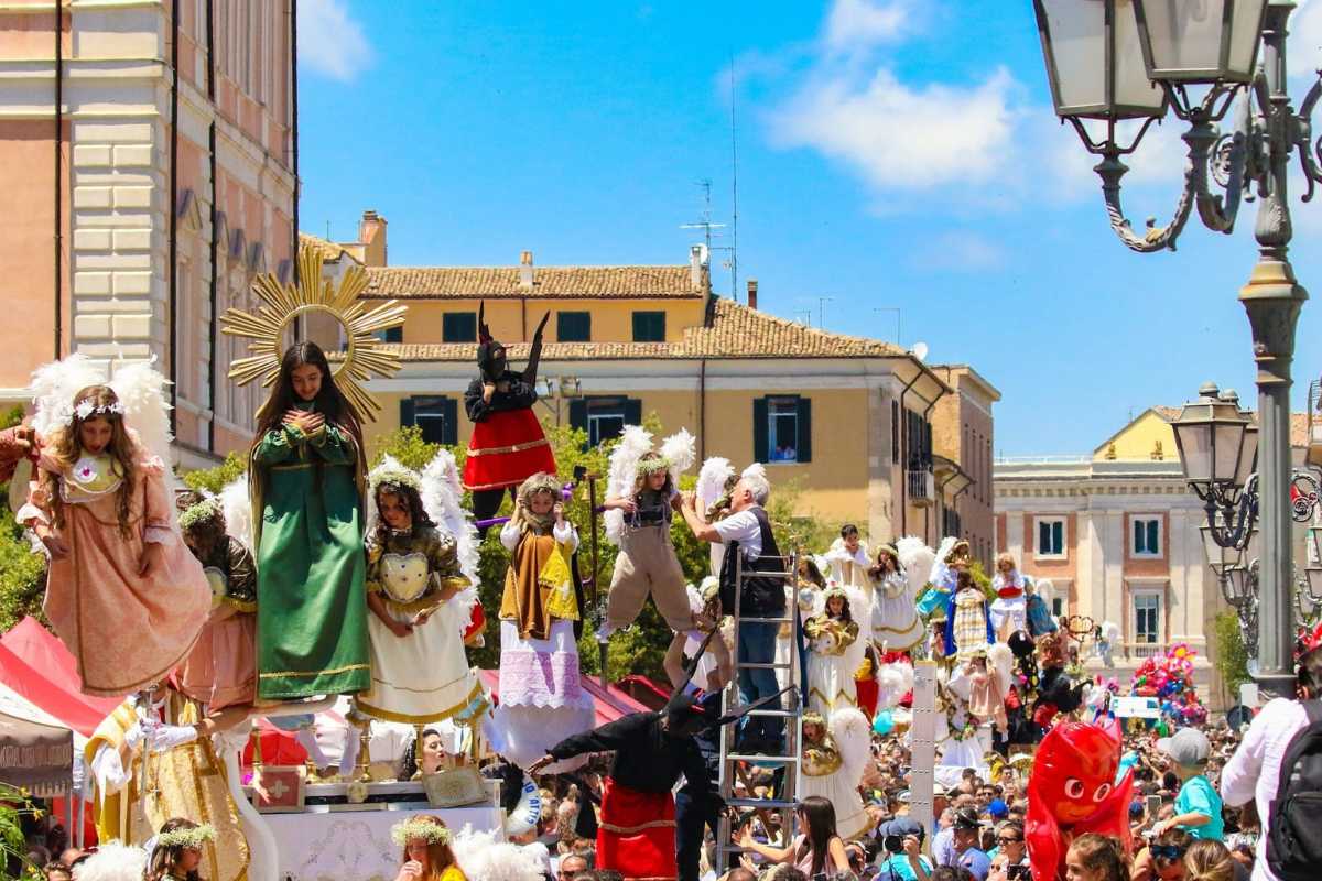 Folla festante durante una tradizionale festa patronale in Italia, con bancarelle e bandiere colorate.