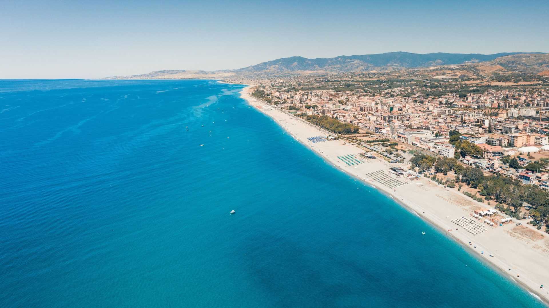 Spiaggia deserta in Calabria, con sabbia dorata e mare cristallino, ideale per una fuga estiva tranquilla.